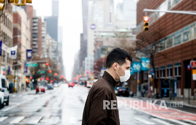 Pria dengan masker melintasi jalan yang sepi di New York, AS, karena pandemi covid-19, ilustrasi