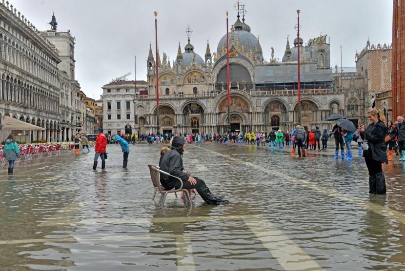 Pria duduk di tengah banjir di Piazza San Marco, Venesia, paad 16 Oktober 2016. Venesia mengalami acqua alta pertamanya tahun ini dengan air naik 93 cm di atas pemukaan laut, menyebabkan sejumlah area banjir.