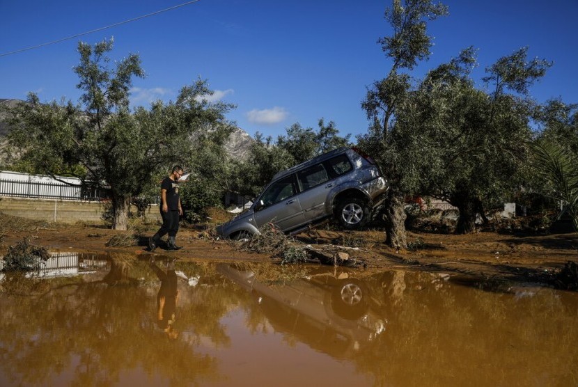 Pria melewati kendaraan yang rusak akibat badai hujan penyebab banjir di Desa Kineta, 68 km dari Athena, Yunani, Senin (25/11).