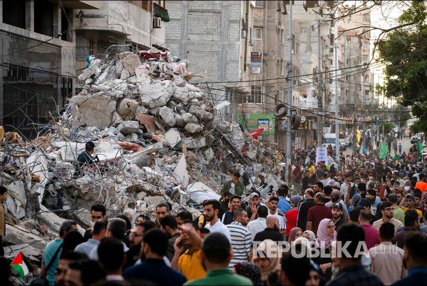  Ratusan warga Gaza berjalan melewati reruntuhan sebuah gedung yang hancur oleh serangan udara Israel, Gaza, Jumat (21/5) waktu setempat. Irak mengumumkan kesiapannya untuk menerima warga Palestina yang terluka selama agresi Israel. 