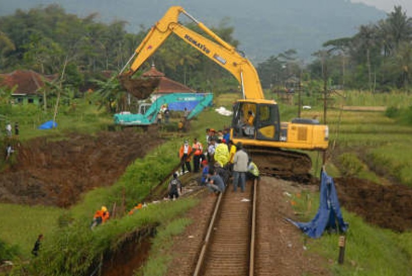 Pekerja menggunakan alat berat memadatkan kembali tanah longsor di perlintasan rel kereta api yang terkena longsor (ilustrasi) 