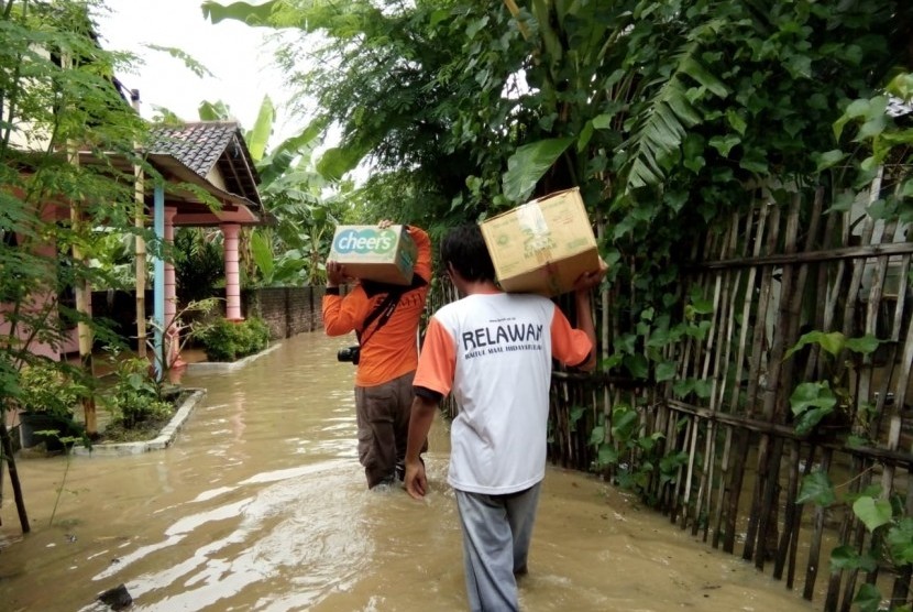 Relawan Laznas BMH memanggul bantuan logistik untuk korban terdampak banjir di Madiun.