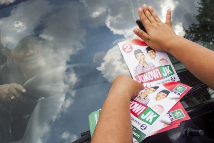 Relawan menempelkan stiker bergambar pasangan capres cawapres Jokowi - Jusuf Kalla 