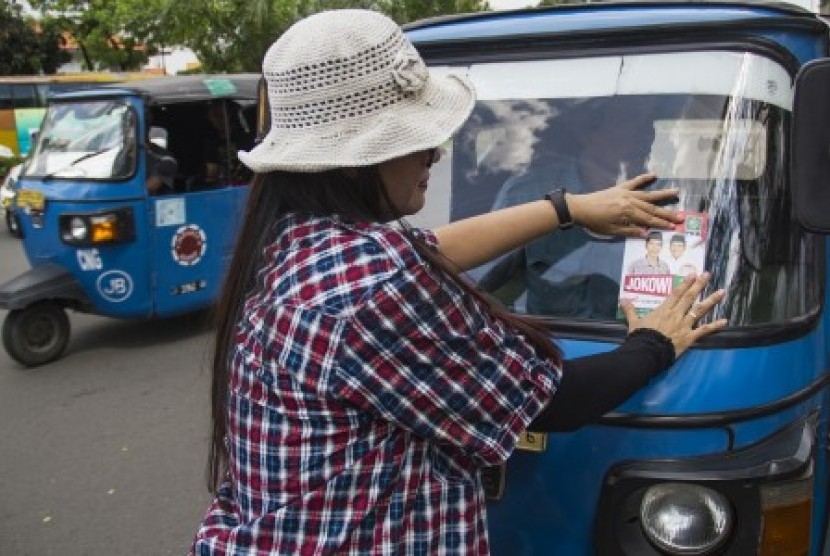 Relawan menempelkan stiker bergambar pasangan capres cawapres Jokowi - Jusuf Kalla 
