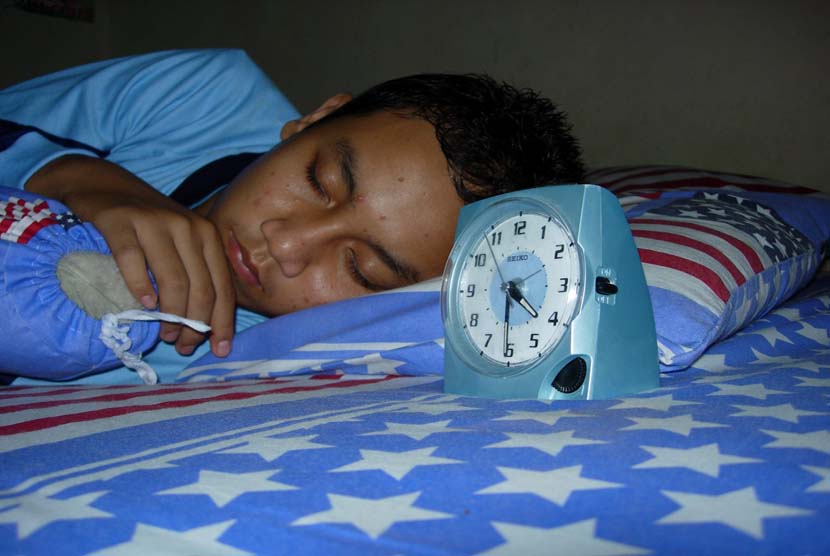  Remaja Laki laki tidur dengan menggunakan jam alarm (ilustrasi).