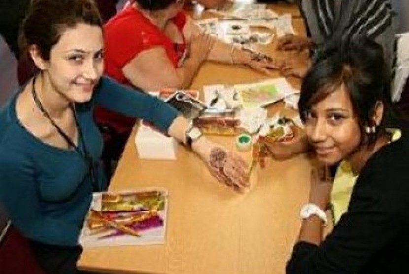 Remaja Muslim melukiskan tato hena di atas tangan remaja non-Muslim Wimbledon, Inggris. Tato henna gratis dan makanan tradisional mewarnai kampanye Ramadhan Muslim kota ini. 
