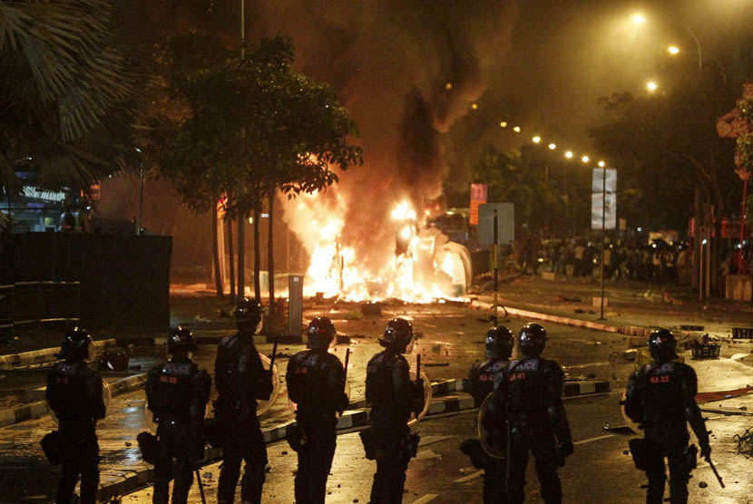 Riot police stand guard as a vehicle goes up in flames after a riot broke out in Singapore's Little India, Sunday (8/12).