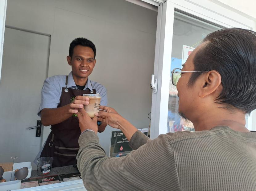Saefudin sedang menyerahkan pesanan minuman kopi kepada pengunjung. 