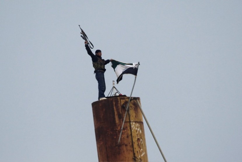 Salah satu anggota pasukan FSA menembakkan senjata ke udara sambil memegang bendera Suriah.