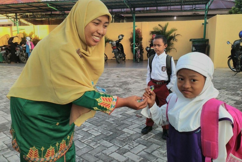 Salah satu guru di PAUD Juara Pekanbaru sedang memberikan permen kepada siswa saat hari pertama sekolah.
