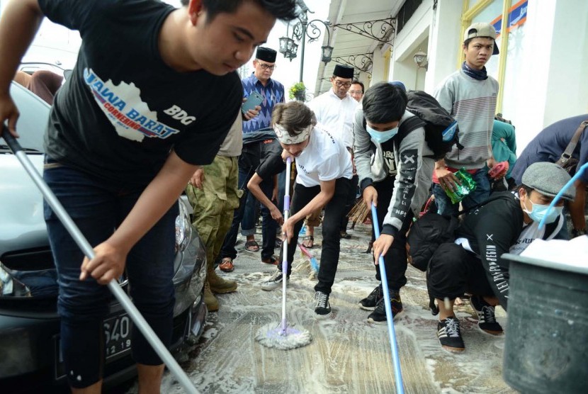 Salah seorang yang merusak fasilitas umum (memakai ikat kepala) menjalani hukuman mengepel Jalan Braga, Kota Bandung, Jumat (1/5). Hukuman tersebut dipantau langsung oleh Wali Kota Bandung Ridwan Kamil. (Republika/Edi Yusuf)