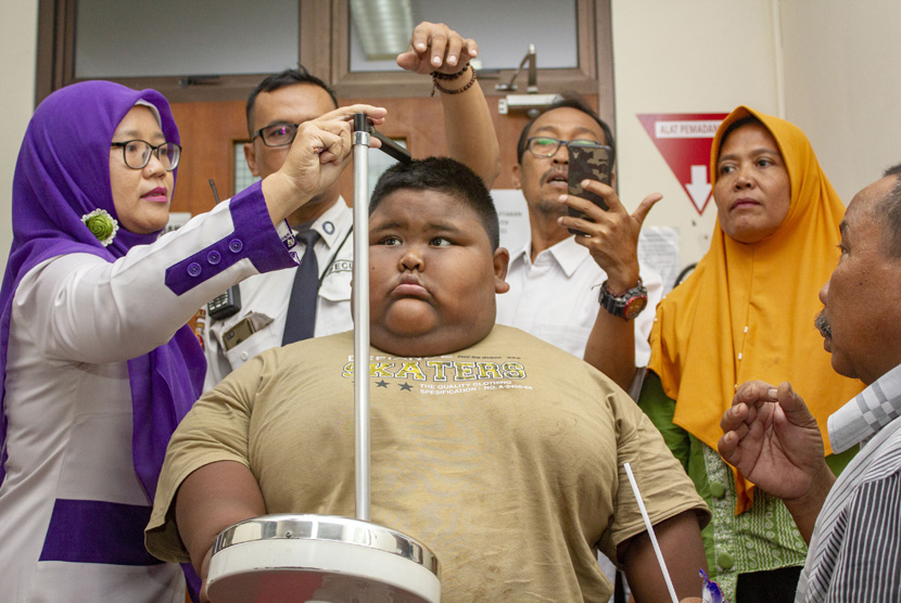Satia Putra (7) penyandang obesitas dengan berat badan mencapai 101 kg dibantu petugas medis dan kedua orangtuanya mengukur tinggi badan sebelum pemeriksaan medis di Rumah Sakit Umum Daerah (RSUD) Karawang, Karawang, Jawa Barat, Rabu (3/7/2019). 