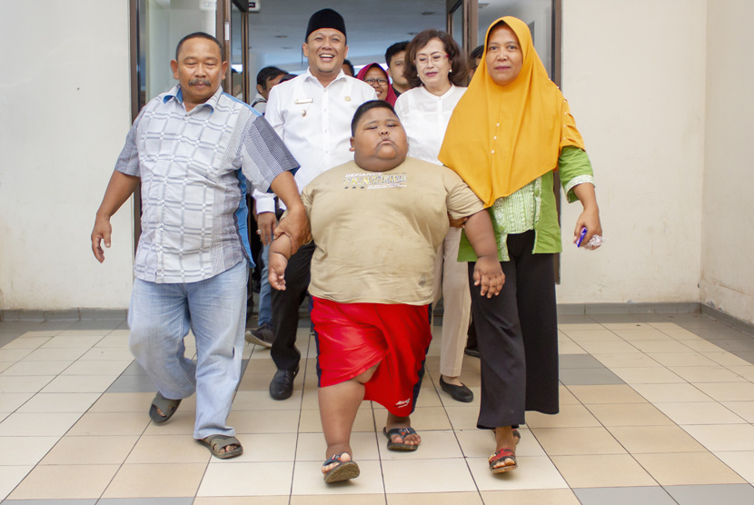 Satia Putra (7) penyandang obesitas dengan berat badan mencapai 101 kg didampingi Wakil Bupati Karawang Ahmad Zamaksyari (kedua kiri) bersama kedua orangtuanya berjalan menuju lokasi pemeriksaan medis di Rumah Sakit Umum Daerah (RSUD) Karawang, Karawang, Jawa Barat, Rabu (3/7/2019). 