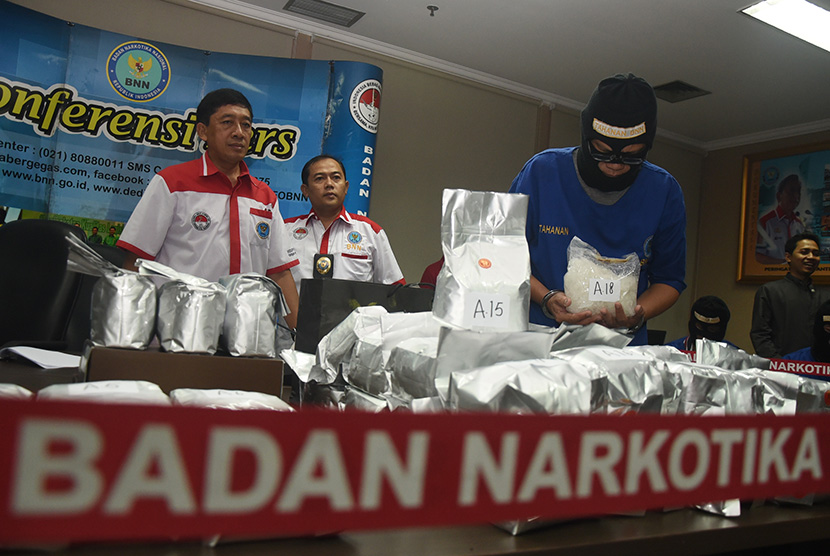 Satu dari empat tersangka memegang barang bukti sabu didampingi Kepala Humas BNN Slamet Pribadi (kiri) saat konferensi pers di Kantor BNN, Jakarta, Ahad (15/3).  (Antara/Hafidz Mubarak)