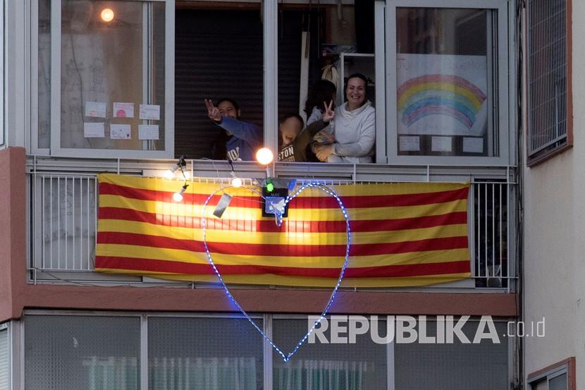 Satu keluarga bertepuk tangan dari balkon mereka selama acara bertepuk tangan yang dijadwalkan secara kolektif untuk menghormati pekerja di sektor sanitasi dan kesehatan di Huesca, Spanyol, Ahad (29/3). 
