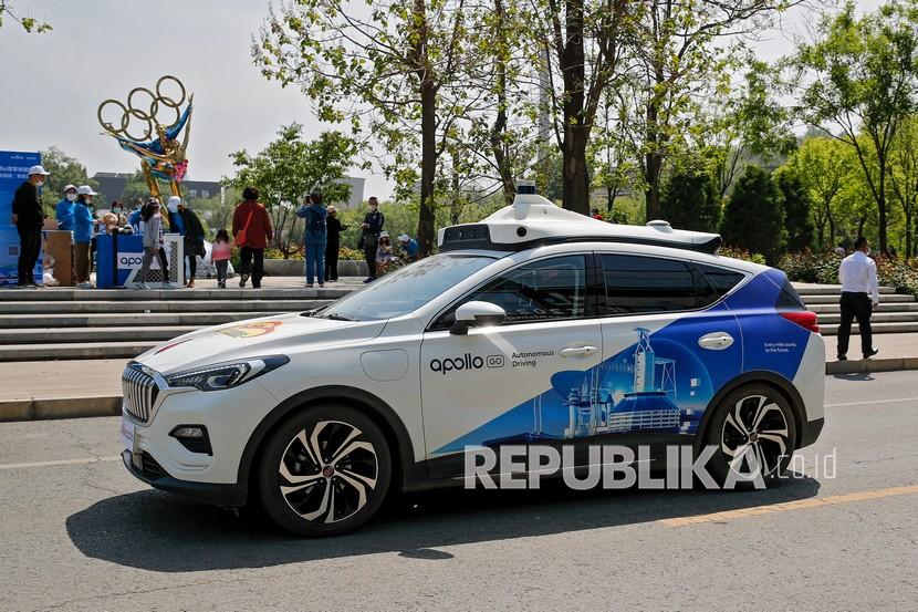 Sebuah Baidu Apollo Robotaxi melewati penyiapan konter layanan pelanggannya di Shougang Park di Beijing, Ahad (2/5). Raksasa teknologi China Baidu meluncurkan layanan taksi tanpa pengemudi berbayar pada hari Ahad, menjadikannya perusahaan pertama yang mengkomersialkan operasi mengemudi otonom di China .