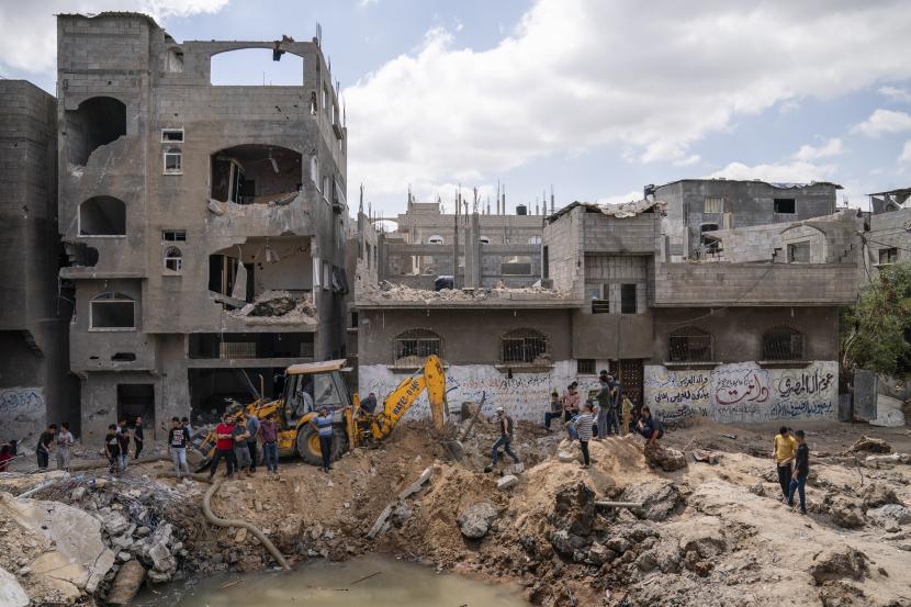 Tetangga berkumpul untuk menyaksikan pembersihan kawah yang penuh dengan air dan limbah setelah rumah Ramez al-Masri dihancurkan oleh serangan udara sebelum gencatan senjata tercapai setelah perang 11 hari antara penguasa Hamas Gaza dan Israel, Ahad, 23 Mei 2021, di Beit Hanoun, Jalur Gaza utara.