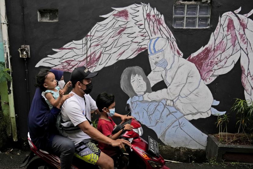  Sebuah keluarga mengenakan masker untuk membantu mengekang penyebaran wabah virus corona mengendarai sepeda motor melewati mural terkait COVID-19. Kenaikan angka kasus kematian akibat virus corona terjadi di Indonesia.