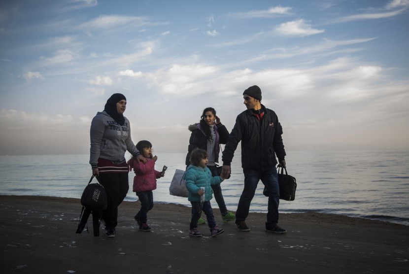 Sebuah keluarga pengungsi berjalan sepanjang pantai setelah melintasi lautan