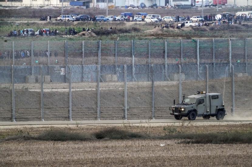 Sebuah kendaraan militer Israel melaju di sepanjang pagar ketika pengunjuk rasa Palestina terlihat di sisi Gaza di perbatasan Israel-Gaza.
