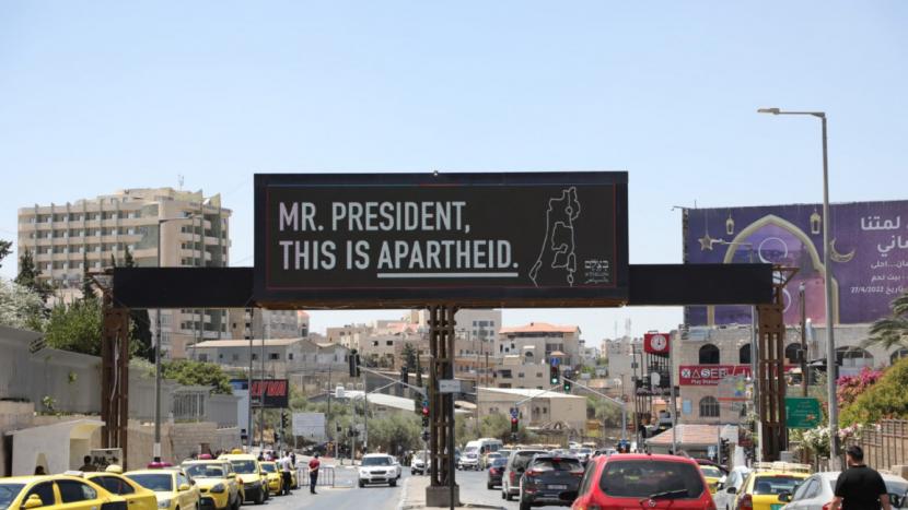 Sebuah papan reklame yang menyatakan Israel adalah negara apartheid telah dipasang oleh kelompok hak asasi manusia BTselem di Tepi Barat yang diduduki. Papan reklame tersebut dipasang menjelang kunjungan Presiden AS Joe Biden ke Timur Tengah, Kamis (14/7/2022). Biden Datang, BTselem Pasang Papan Reklame Ingatkan Perilaku Apartheid Israel