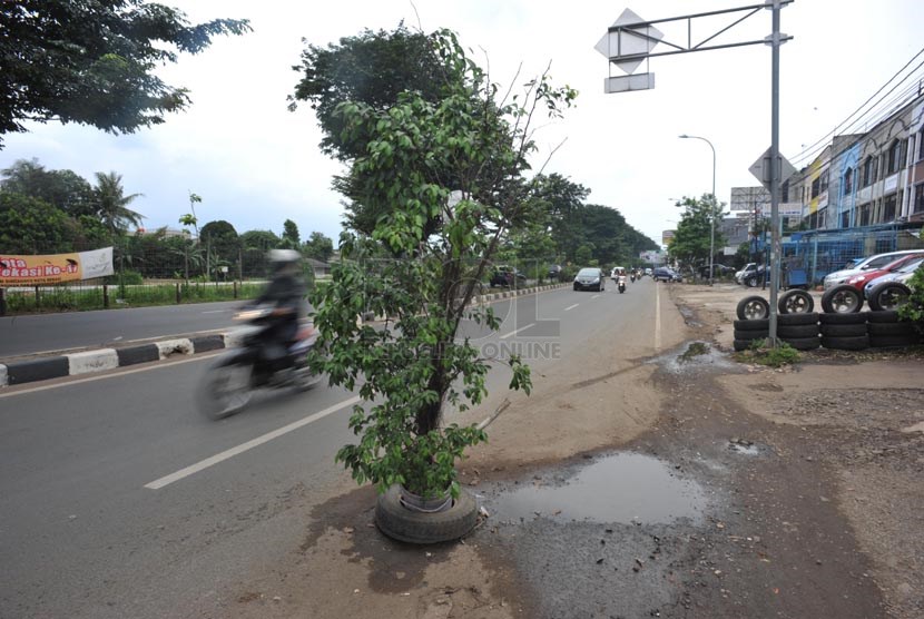 Sebuah pohon dipasang untuk menutupi lubang jalanan di jalan kalimalang, bekasi, jawa barat, Selasa (25/4).