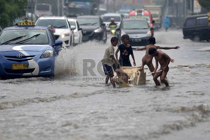   Sejumlah anak bermain air saat banjir di Jalan Gunung Sahari, Jakarta, Ahad (12/1). (Republika/Agung Supriyanto)