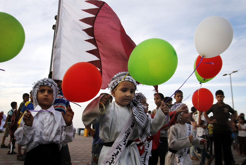   Sejumlah anak Palestina memegang balon berwarna bendera Qatar sambil menunggu konvoi Emir Qatar Sheikh Hamad bin Khalifa al-Thani yang akan melewati jalan di Kota Gaza, Palestina, Selasa (23/10).  (Hatem Moussa/AP)
