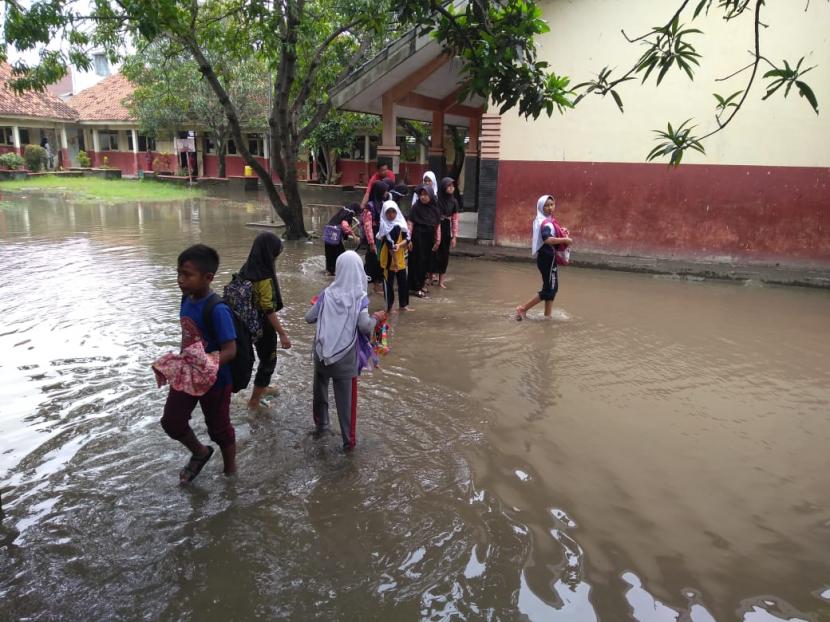 Sejumlah anak sekolah di SDN 2 Widasari dan SDN 3 Widasari, Kabupaten Indramayu berjalan melewati banjir yang menggenangi halaman sekolah mereka, Rabu (25/1/2023). 