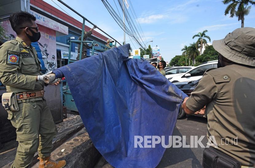 Personel Satuan Polisi Pamong Praja membongkar kios liar yang berjualan di trotoar.