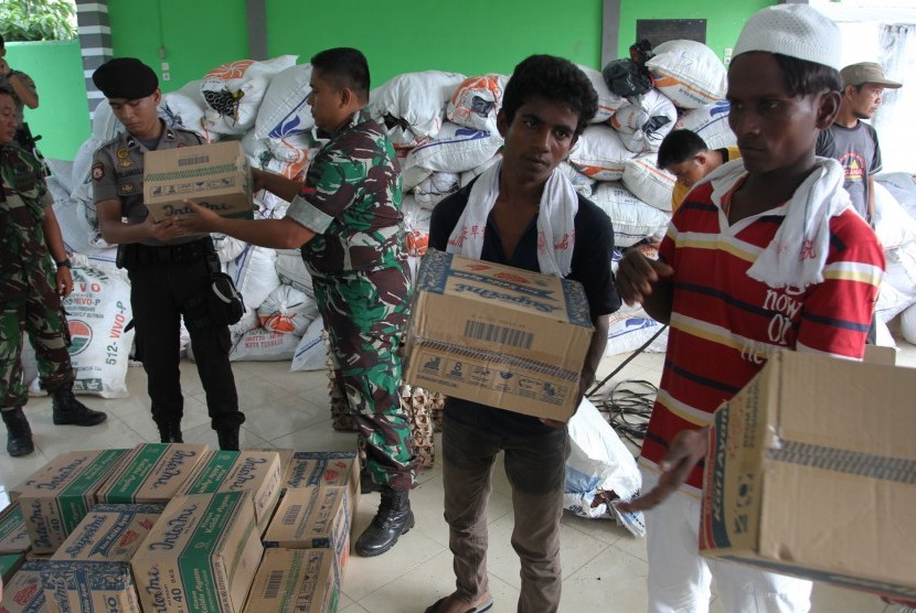 Sejumlah imigran etnis Rohingya, Myanmar dan Bangladesh dibantu personel TNI dan Polri mengangkat barang bantuan warga, ketika dilakukan proses pemindahan dari penampungan sementara, Pangkalan Susu, Langkat, Sumatera Utara, Senin (18/5).