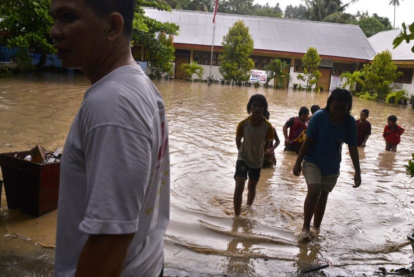 Sejumlah murid sekolah dasar berjalan menembus banjir yang menggenangi sekolah mereka di kawasan permukiman Kecamatan Singkil, Manado, Sulawesi Utara, Jumat (21/10).