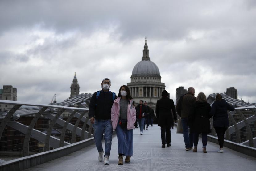 Sejumlah orang berjalan di Millenium Bridge dengan latar Katedral St Paul di London, Inggris, Selasa (10/3). Jumlah kematian akibat virus corona di Inggris mencapai enam orang.(AP Photo/Matt Dunham)
