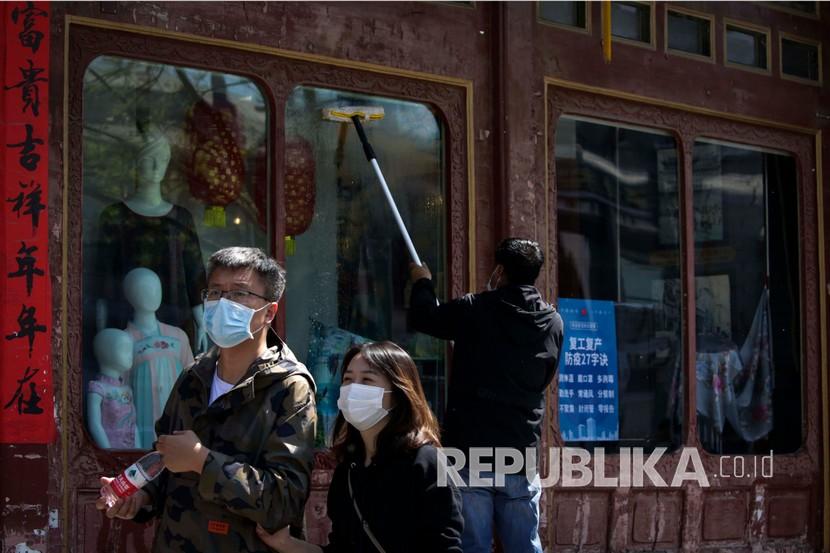 Sejumlah orang berjalan melewati pekerja yang membersihkan jendela di sebuah toko pakaian di Beijing. Pemerintah Cina telah meminta perusahaan perdagangan dan pengolahan makanan untuk meningkatkan stok biji-bijian dan minyak sayur. 