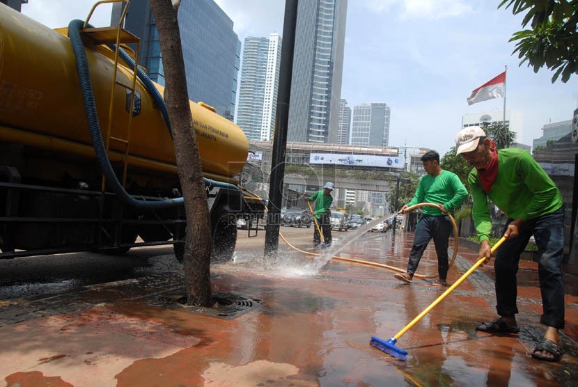 Sejumlah pekerja membersihkan lumpur sisa banjir di pedestrian jalan protokol Sudirman, Jakarta Pusat, Sabtu (19/1). (Republika/Agung Fatma Putra)