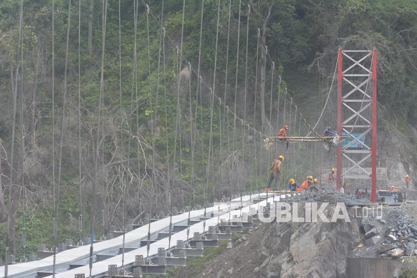 Sejumlah pekerja menyelesaikan pembangunan jembatan gantung Gladak Perak di Lumajang, Jawa Timur, Sabtu (9/4/2022). Kementerian Pekerjaan Umum dan Perumahan Rakyat membangun jembatan gantung darurat tersebut untuk dilewati sementara oleh kendaraan roda dua, sebelum jembatan permanen yang rusak akibat awan panas guguran Gunung Semeru kembali dibangun. 