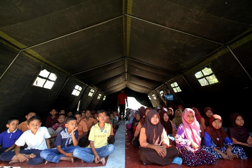 Sejumlah pelajar Madrasah Ibtidaiyah Negeri (MIN) mengikuti proses belajar mengajar di tenda darurat pasca sekolah mereka roboh akibat gempa 6,5 SR di Desa Paru Keude, Kecamatan Bandar Baro, Pidie Jaya, Aceh, Jumat (16/12). 