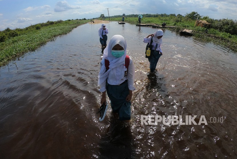Sejumlah pelajar melewati jalan penghubung Desa Jebus dengan Desa Gedong Karya yang terendam banjir luapan Sungai Batanghari di Muarojambi, Jambi.