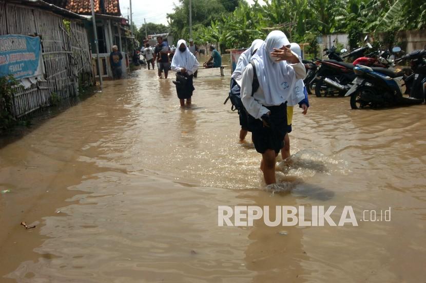 Sejumlah pelajar melintasi genangan air saat terjadi banjir di Kelurahan Pesurungan, Tegal, Jawa Tengah, Selasa (23/11/2021). Curah hujan tinggi dan buruknya drainase mengakibatkan ratusan rumah di sejumlah wilayah Kota Tegal terendam banjir.