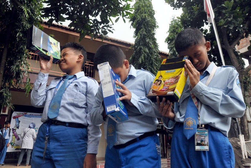 Sejumlah pelajar mengamati pergerakan sinar matahari menggunakan teropong kardus bekas saat dilakukan percobaan pembuatan teropong gerhana matahari di SD Muhammadiyah I Magelang, Temanggung, Jawa Tengah, Senin (7/3). 