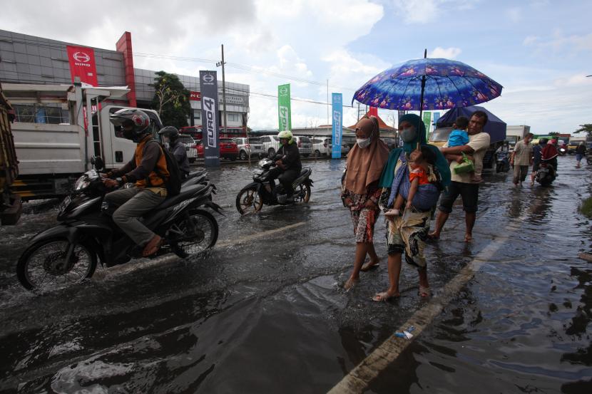 Sejumlah pengendara kendaraan bermotor dan pejalan kaki melintasi genangan air di Surabaya (ilustrasi)