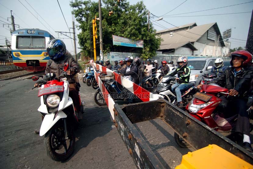 Sejumlah pengendara sepeda motor menunggu di depan pintu perlintasan kereta api kawasan Kalibata, Jakarta Selatan.( Republika/Raisan Al Farisi)