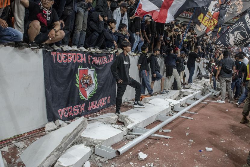 Sejumlah penonton berdiri di atas puing pagar pembatas yang roboh saat peresmian Stadion Jakarta International Stadium (JIS) di Jakarta, Ahad ( 24/7/2022). Pagar pembatas penonton zona utara JIS roboh karena tidak dapat menahan beban orang yang duduk dan bersandar di pagar tersebut. 