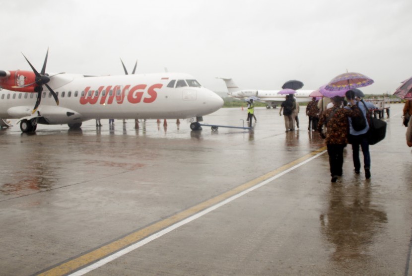 Sejumlah penumpang pesawat menggunakan payung berjalan menuju pesawat di Bandara El Tari Kupang, NTT Kamis, (28/12/18).