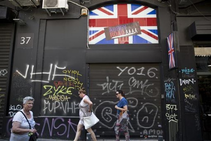 Sejumlah perempuan berjalan melewati sebuah toko memasang bendera Inggris di Athena, Yunani, 24 Juni 2016.