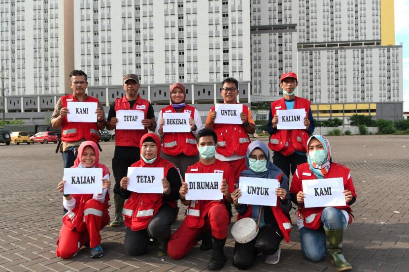 Sejumlah petugas Palang Merah Indonesia (PMI) membawa tulisan Kami Tetap Bekerja Untuk Kalian, Kalian Tetap di Rumah Untuk Kami di Wisma Atlet, Kemayoran, Jakarta, Sabtu (21/3/2020). (Antara/M Risyal Hidayat)