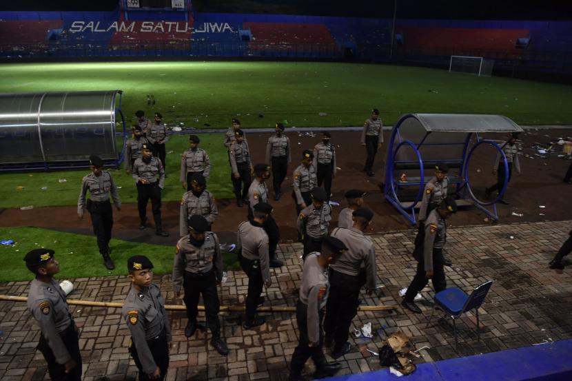 Sejumlah polisi melintas di pinggir lapangan Stadion Kanjuruhan, Malang, Jawa Timur, Ahad (2/10/2022). Kerusuhan yang terjadi di stadion tersebut menyebabkan 13 unit mobil rusak, 10 unit diantaranya mobil polisi dan tiga unit mobil pribadi. 