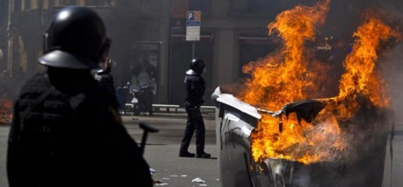 Sejumlah polisi Spanyol berdiri dekat tong sampah terbakar. Terjadi bentrok antar massa protes dengan aparat dan aksi kekerasan dalam demonstrasi yang berujung rusuh di Barcelona