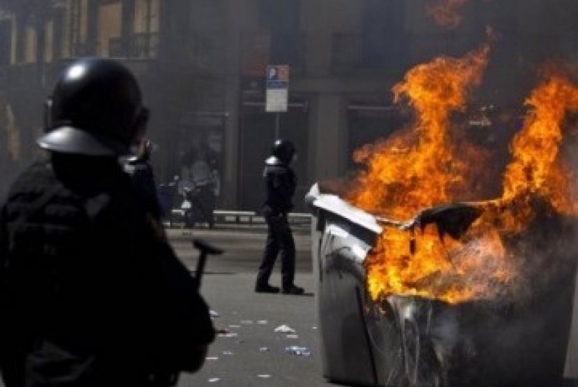 Sejumlah polisi Spanyol berdiri dekat tong sampah terbakar. Terjadi bentrok antar massa protes dengan aparat dan aksi kekerasan dalam demonstrasi yang berujung rusuh di Barcelona