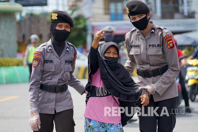 Sejumlah polwan menuntun seorang nenek menyeberang jalan saat pembagian masker gratis.